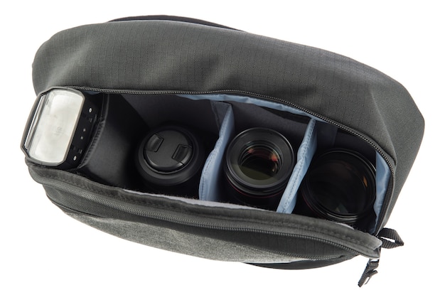 Isolated close up studio shot of small black and gray professional photographer shockproof waterproof fabric camera zipper bag contains flash and lens in soft compartment divider on white background.