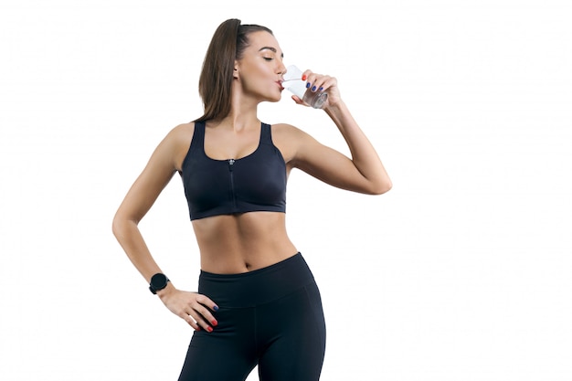 Isolated portrait of young woman in sportswear drinking water