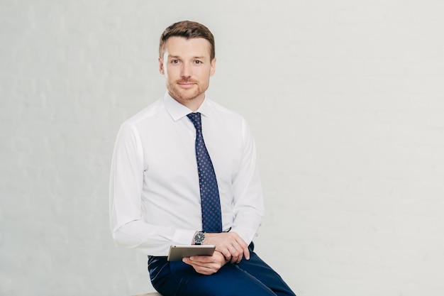 Isolated shot of successful male manager wears elegant white shirt black trousers and tie uses modern tablet computer for work and entertainement isolated over white background Business concept