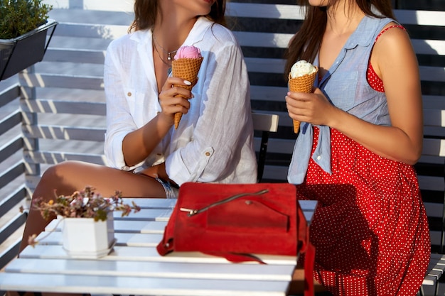 Isolated view of two female friends sitting and holding two ice cream cones in their hands at