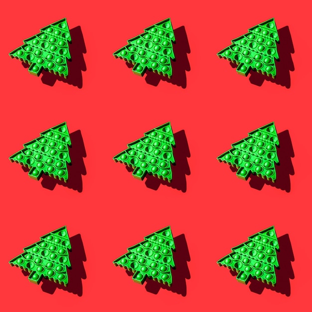 Isometric seamless pattern of green kids anti stress pop it toy in form of Christmas tree on red