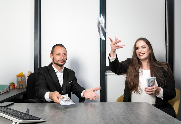 Israeli woman throwing out money banknotes while sitting in office and Bearded Jewish man in Yarmulke sit at desk looking up catching money hundred dollar bills Businessman catching falling money