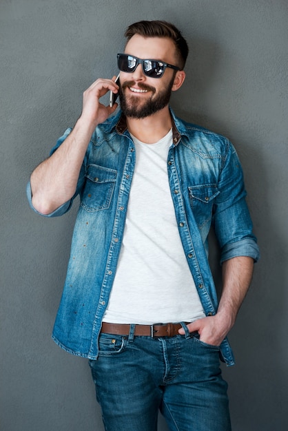 It is great to hear from you!Smiling young man talking on the mobile phone and looking away while standing against grey background