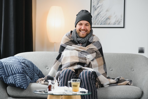 It's cold at home in wintertime Man freezing in his house in winter because of broken thermostat young guy wrapped in woolen plaid shivering while sitting on sofa in living room interior