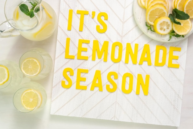 It's lemonade season wood sign with freshly sliced lemons on a wood cutting board.