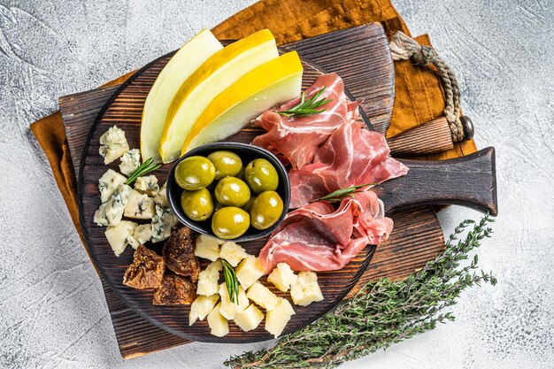 Italian appetizer platter antipasti snack with Prosciutto ham Parmesan Blue cheese Melon and Olives on wooden board White background Top view