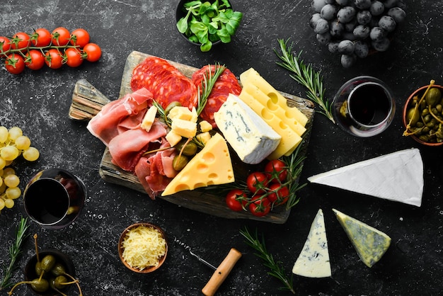 Italian appetizers Cheese wine salami and prosciutto on a black stone background Top view Free space for your text