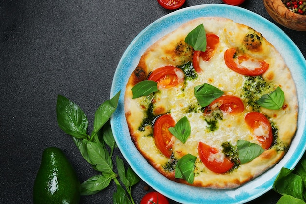 Italian bread focaccia with tomatoes, basil and sea salt on dark concrete bakground, top view.