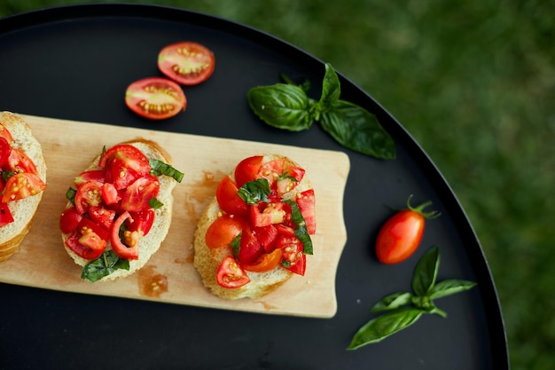 Italian bruschetta with fresh red tomatoes and basil herbs on a wooden board outdoor