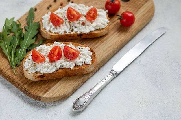 Italian bruschetta with roasted tomatoes, mozzarella cheese and herbs on a cutting board.