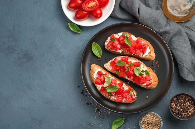 Italian bruschetta with tomatoes, cream cheese and basil on a dark gray-blue background. Top view, copy space.