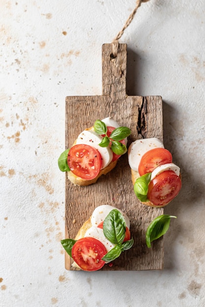 Italian bruschetta with tomatoes mozzarella and basil on rustic wooden board top view