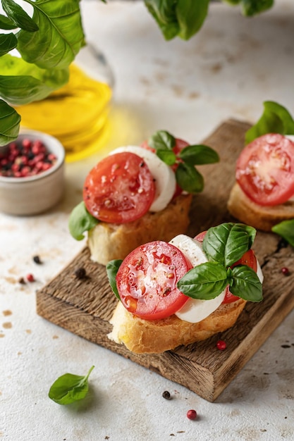 Italian bruschetta with tomatoes mozzarella on rustic wooden board with basil greens in blur and ingredients