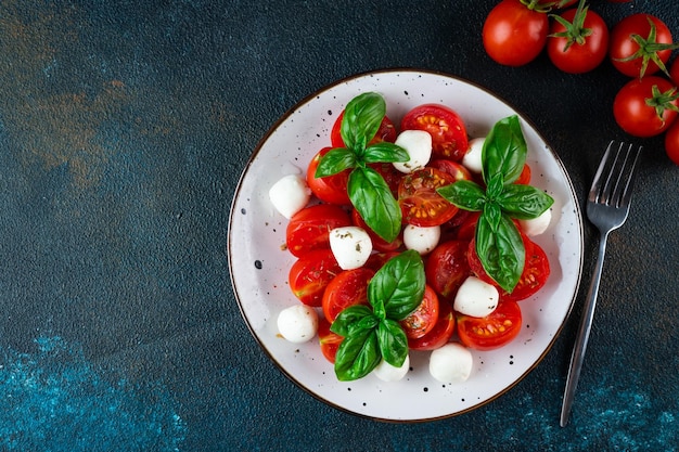 Italian caprese salad with sliced tomatoes mozzarella basil olive oil on a dark background Top view Italian food Healthy salad Summer food