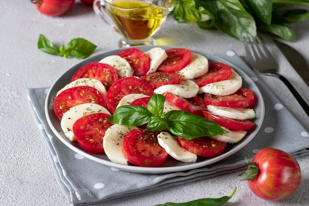 Italian caprese salad with sliced tomatoes mozzarella cheese basil and olive oil on light gray background