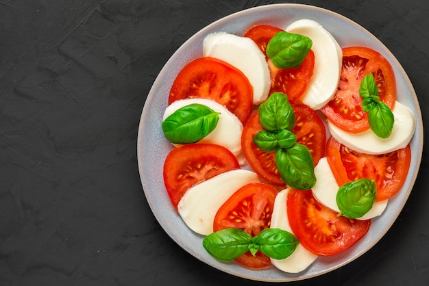 Italian caprese salad with sliced tomatoes, mozzarella cheese, basil, olive oil in a plate