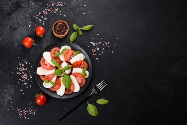 Italian caprese salad with sliced tomatoes, mozzarella cheese, basil, olive oil. Served in vintage black plate on a dark concrete background