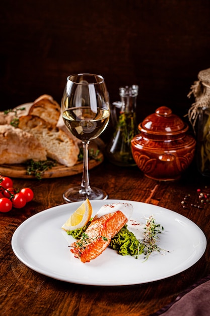 Italian Cuisine. Red fish steak, salmon with lemon, a side dish of spinach. Beautiful restaurant serving in a white plate with a glass of white wine