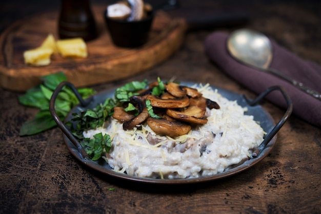 Italian dish risotto with mushrooms, Parmesan and herbs. Risotto in a copper plate on a wooden brown background