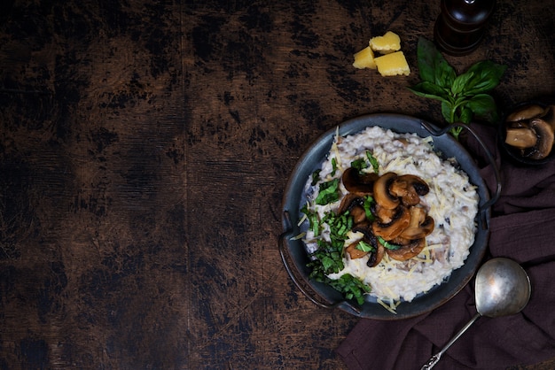 Italian dish risotto with mushrooms, Parmesan and herbs. Risotto in a copper plate on a wooden brown background