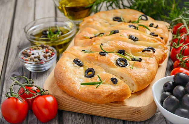 Italian focaccia bread with olives and rosemary on rustic wooden background.