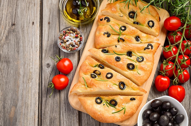 Italian focaccia bread with olives and rosemary on rustic wooden background.