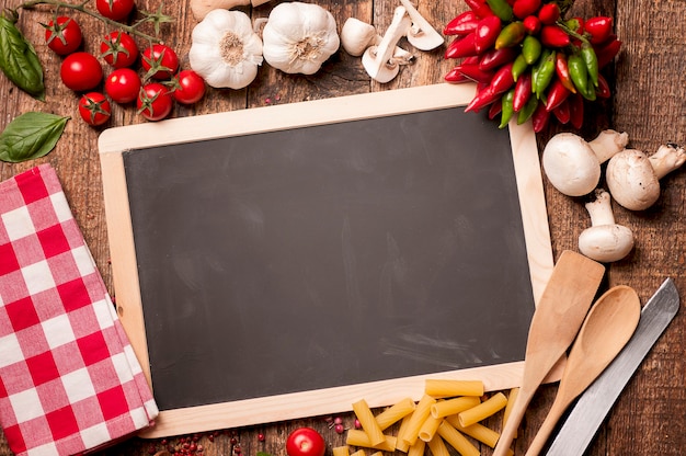 Italian food cooking. Tomatoes, basil, pasta and blackboard for your recipe on stone kitchen table. Top view with copy space