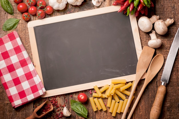 Italian food cooking. Tomatoes, basil, pasta and blackboard for your recipe on stone kitchen table. Top view with copy space