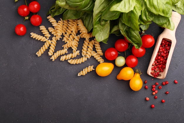 Italian food: pasta, basil, tomato, olive oil on a black background, copy space.