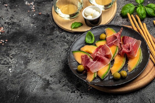 Italian food with red wine melon and prosciutto Cantaloupe melon with prosciutto or jamon and green basil leaves with glass of wine Restaurant menu Antipasti appetizer cookbook recipe top view