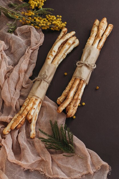 Italian grissini or salted bread sticks on brown background with flowers and beige cloth