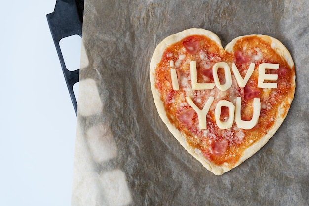 Italian heart shaped pizza with salami tomato sauce parmesan pizza sauce mozzarella and olive oil on parchment paper with cheese I love you Love concept for Valentine's Day February 14