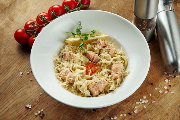 Italian homemade tagliatelle with salmon and parmesan in a beige bowl on a wooden surface. Tasty pasta. Copy space