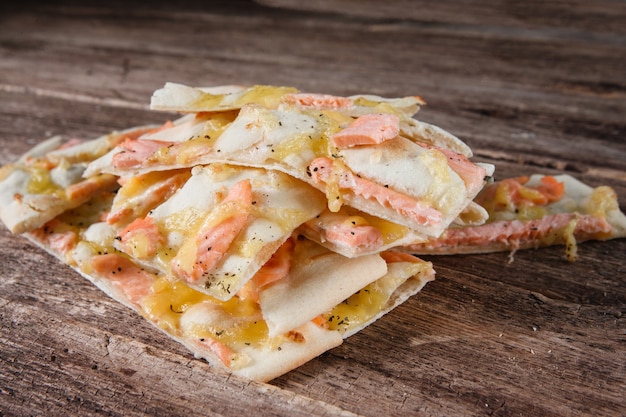 Italian national cuisine, fast food. Appetizing slices of hot pizza with seafood on rustic wooden table, close up.