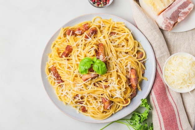 Italian pasta carbonara made of spaghetti, bacon, parmesan cheese and basil in a plate on white marble table