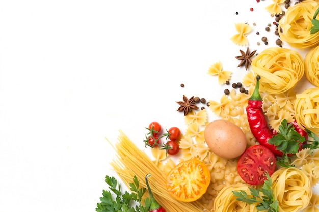 Italian pasta of different kinds with spices, red hot pepper, chicken eggs, yellow and red tomatoes on a white stone background. Concept cooking Italian pasta and sauce.