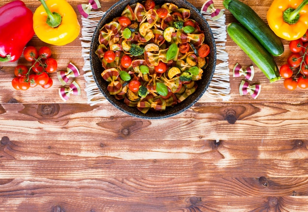 Italian pasta farfalle in tomato sauce and various type of vegetables on a wooden background, free space for text.