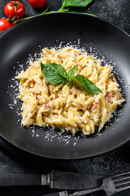 Italian pasta Orzo. Recipe with cream sauce, bacon and Basil. Prepared risoni. Black wooden background. Top view