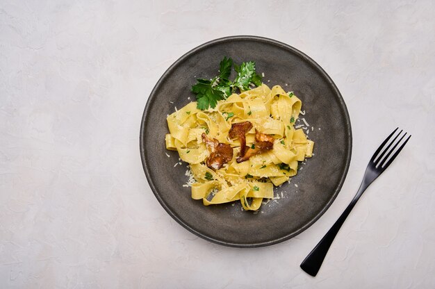 Photo italian pasta pappardelle with mushrooms chanterelles cheese and parsley on dark plate with black