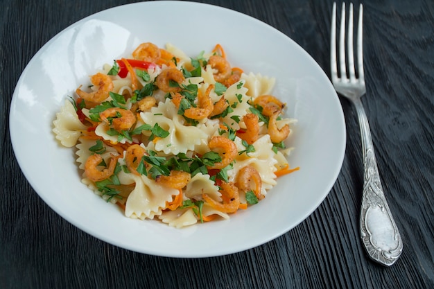 Italian pasta in a sauce with shrimps on a plate, top view. Dark wooden background. Space for text.