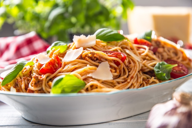 Italian pasta spaghetti bolognese in white bowl with tomatoes parmesan cheese and basil.