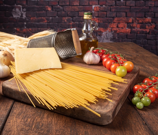 Italian pasta, spaghetti, tomatoes, olive oil, cheese and spices on rustic wood