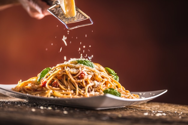 Italian pasta spaghetti with tomato sauce basil and parmesan cheese in white plate.