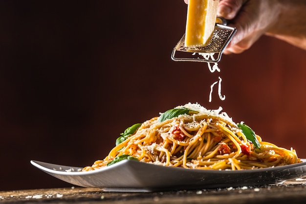 Italian pasta spaghetti with tomato sauce basil and parmesan cheese in white plate.