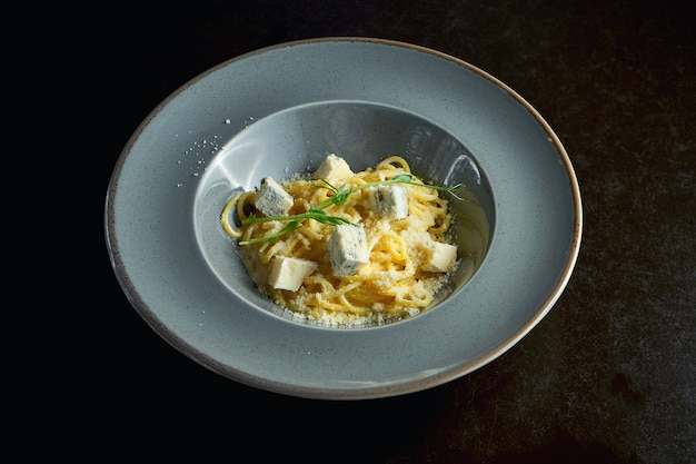 Italian pasta with three types cheese of parmesan, brie and blue mold in a gray plate on a black background. Close up, selective focus