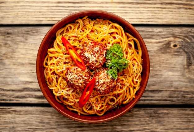 Italian pasta with tomato sauce and meatballs in a plate with spices on wood