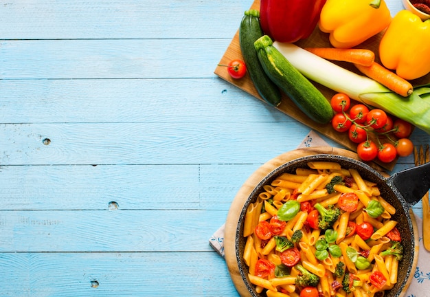 Italian penne pasta in tomato sauce and different type of vegetables, on wooden table