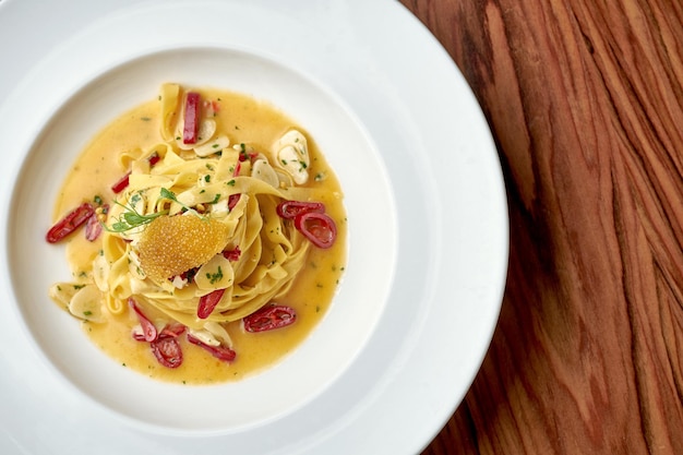 Italian Pepperoncini Pasta with garlic, hot pepper and pike caviar in a white plate on a wooden background