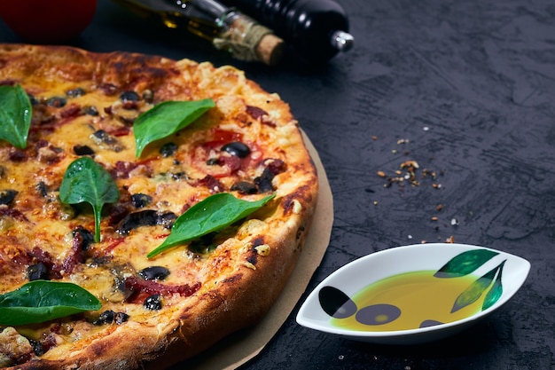 Italian pizza and cooking ingredients on dark background Tomatoes olives oil herbs and spices