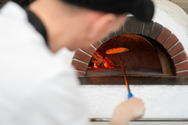 Italian pizza is cooked in a woodburning oven The cook puts the pizza in the oven on a shovel